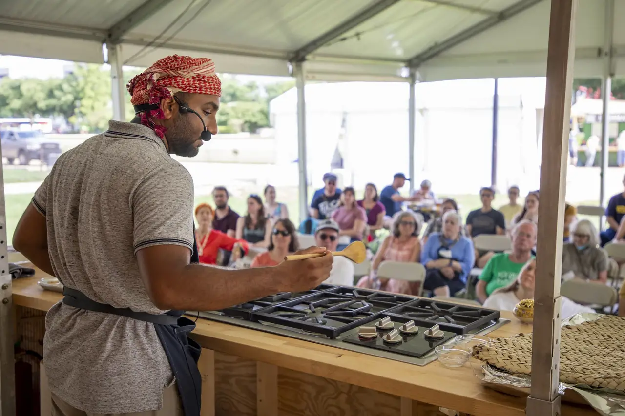 Mommin Al Rawahi standing in front of a stovetop on stage, facing a crowd