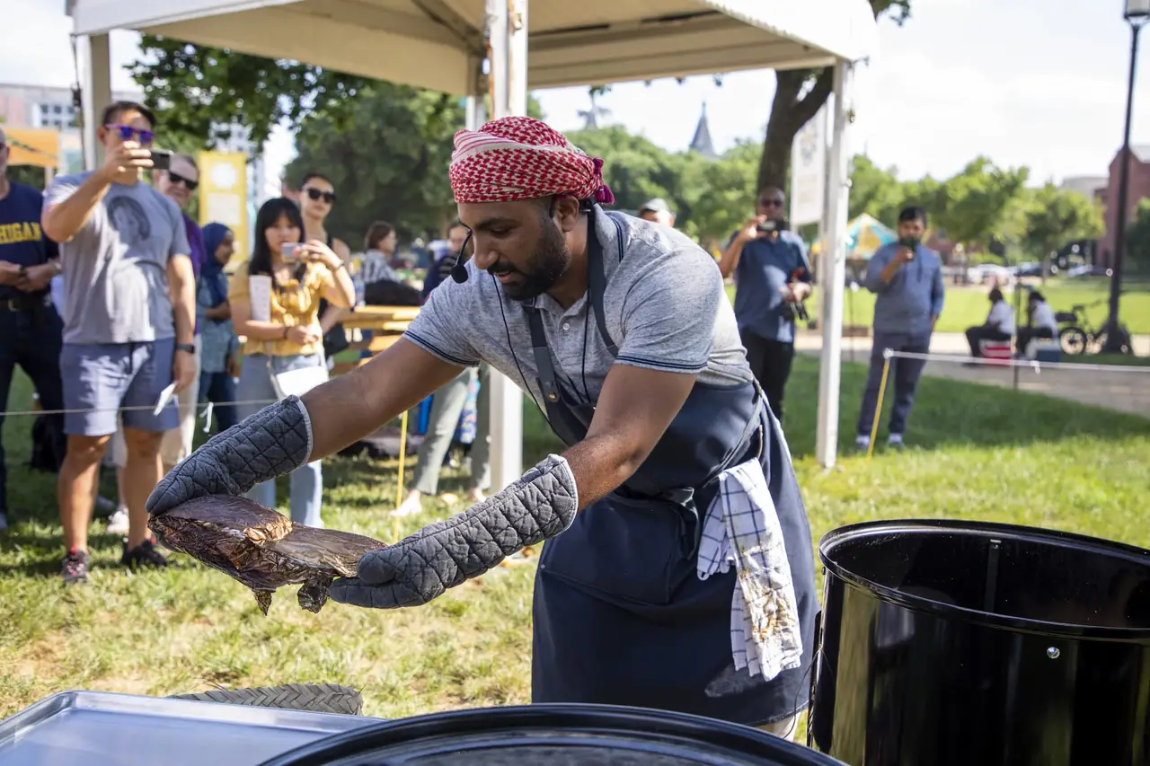 Mommin Al Rawahi using oven mitts to place a foil-wrapped package on a serving tray