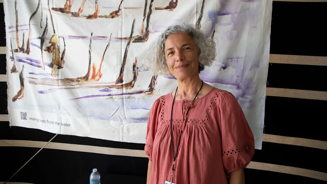 Zahidah Zeytoun Millie standing in front of a large canvas that she painted with mangrove trees