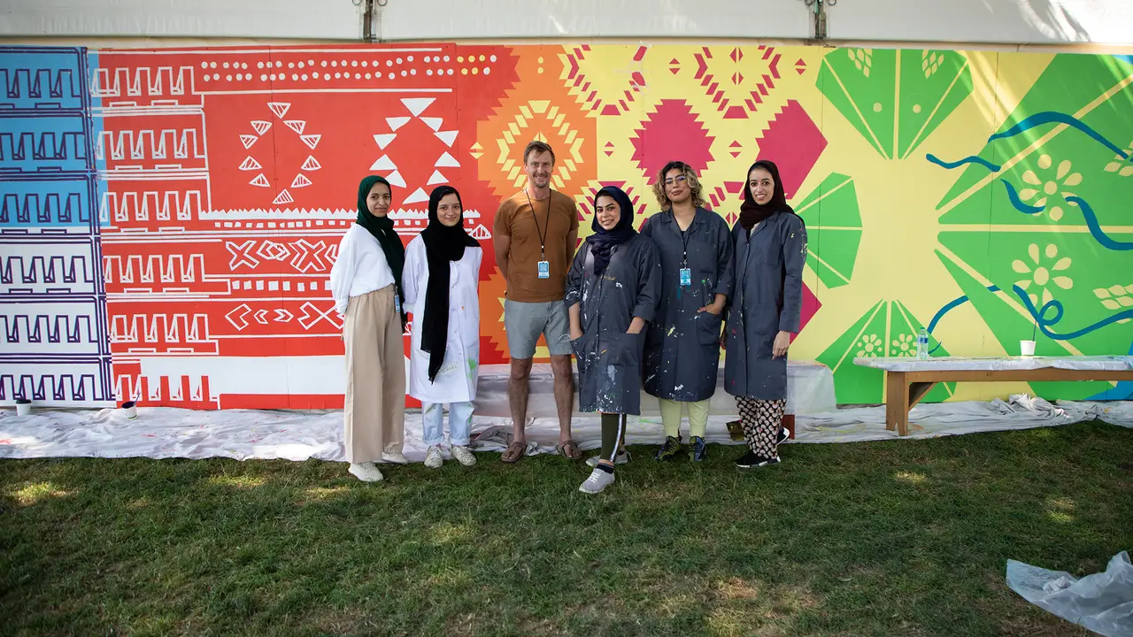 Group of people posing in front of a colorful, hand-painted mural