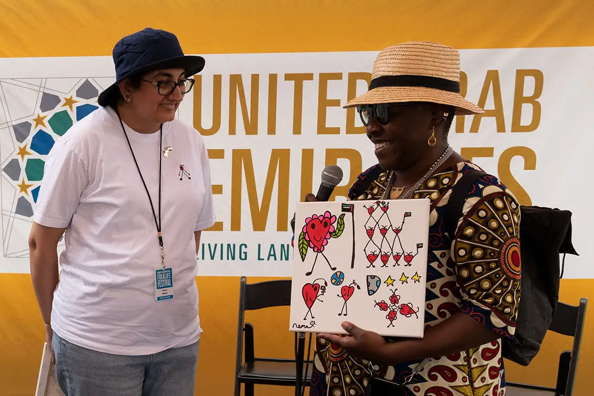 Two women on stage, one holding a microphone and a colorful piece of art